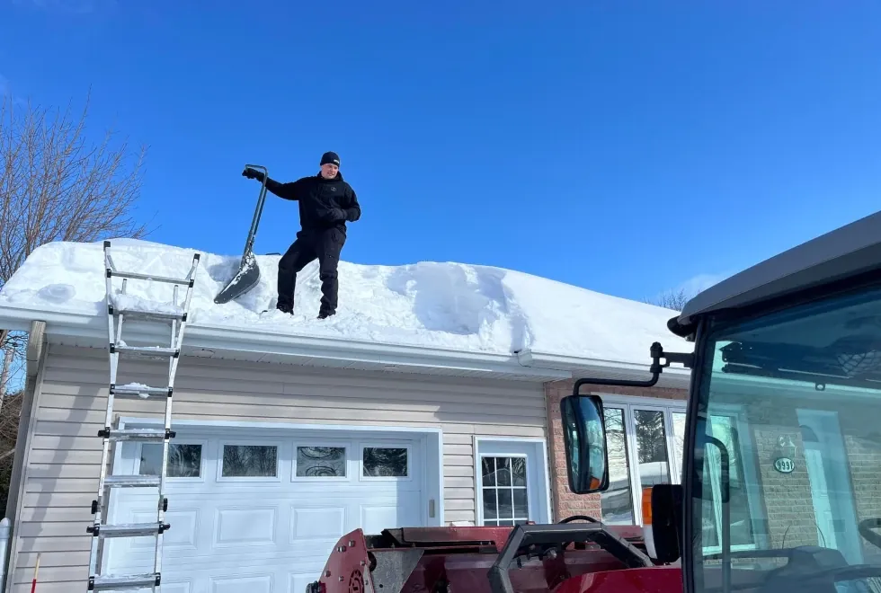 Un employé d’À Point déneigement qui déneige le toit d’une maison.