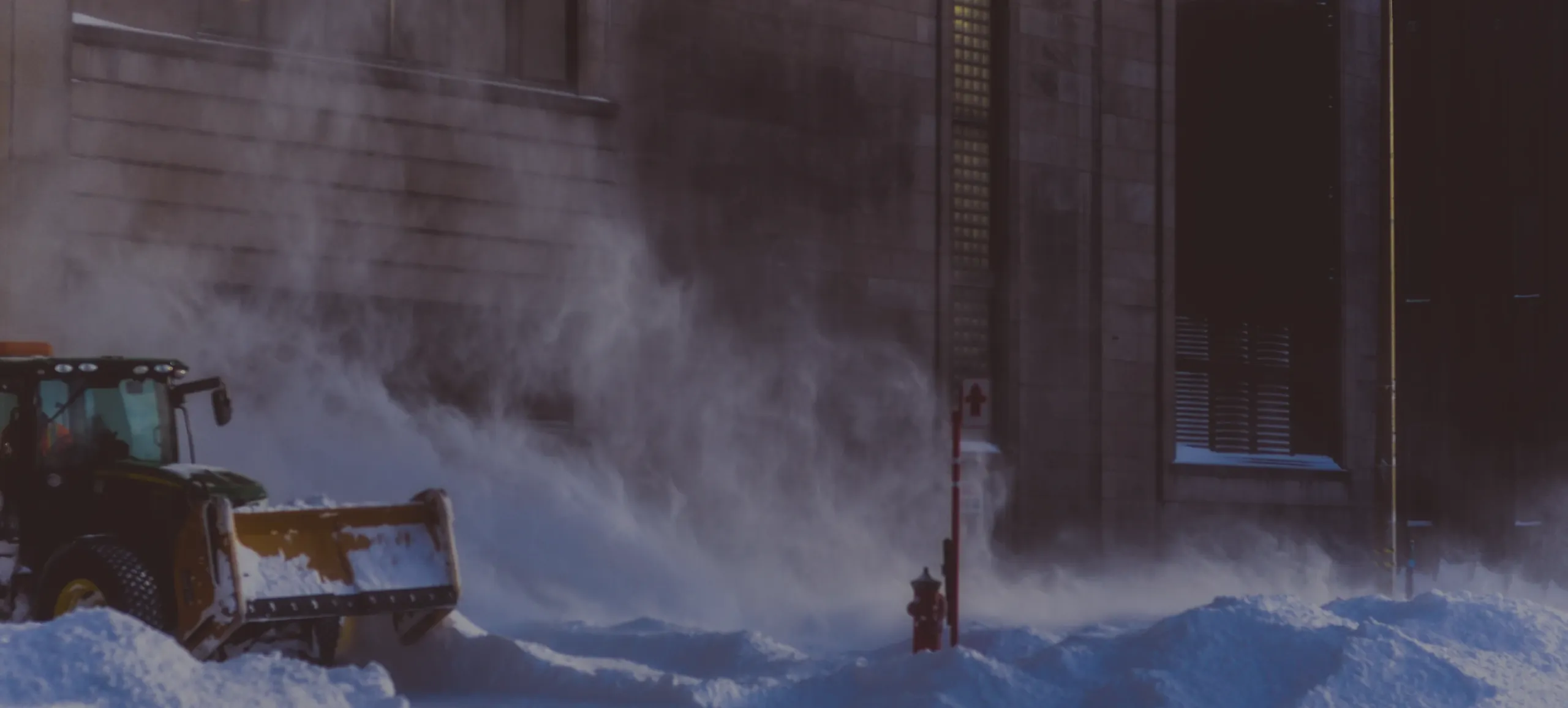 Un tracteur déneigeur qui souffle la neige devant un immeuble.