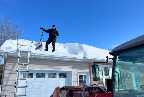 Un employé d’À Point déneigement qui déneige le toit d’une maison.